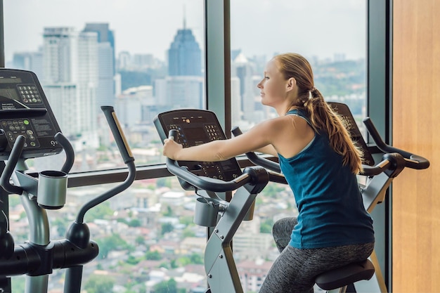 Jeune femme sur un vélo stationnaire dans une salle de sport sur fond de grande ville