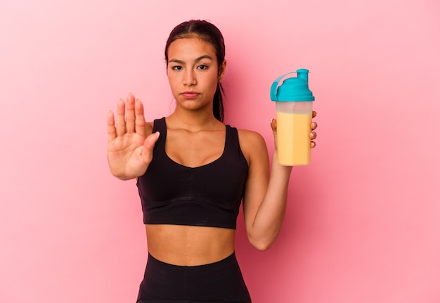 Jeune femme vénézuélienne buvant un shake protéiné isolé sur fond rose debout