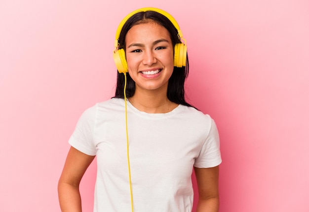 Jeune femme vénézuélienne écoutant de la musique isolée sur fond rose heureuse souriante et joyeuse