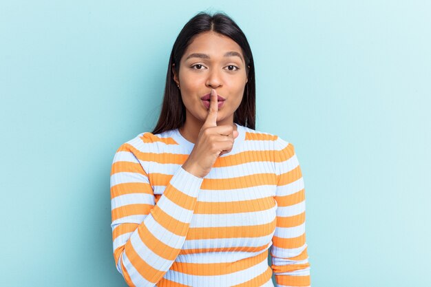 Jeune femme vénézuélienne isolée sur fond bleu gardant un secret ou demandant le silence.