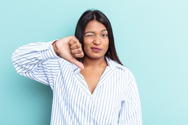 Jeune femme vénézuélienne isolée sur fond bleu montrant un geste d'aversion, les pouces vers le bas. Notion de désaccord.