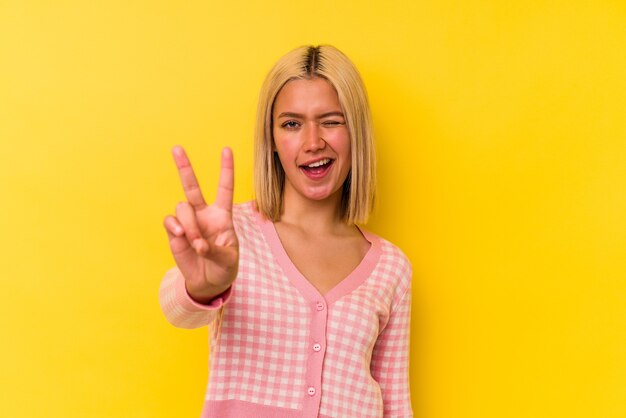 Jeune femme vénézuélienne isolée sur fond jaune montrant le numéro deux avec les doigts.
