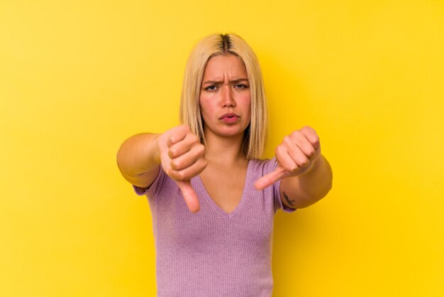 Jeune femme vénézuélienne isolée sur fond jaune montrant le pouce vers le bas et exprimant son aversion.