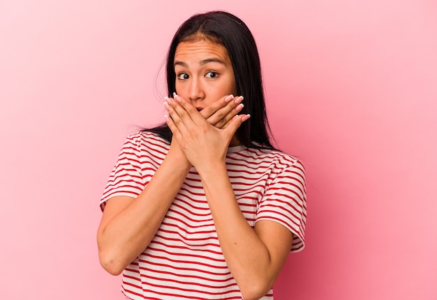 Jeune femme vénézuélienne isolée sur fond rose couvrant la bouche avec les mains à l'air inquiet.