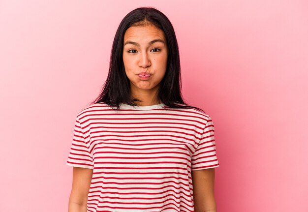 Jeune femme vénézuélienne isolée sur fond rose souffle les joues, a une expression fatiguée. Concept d'expression faciale.