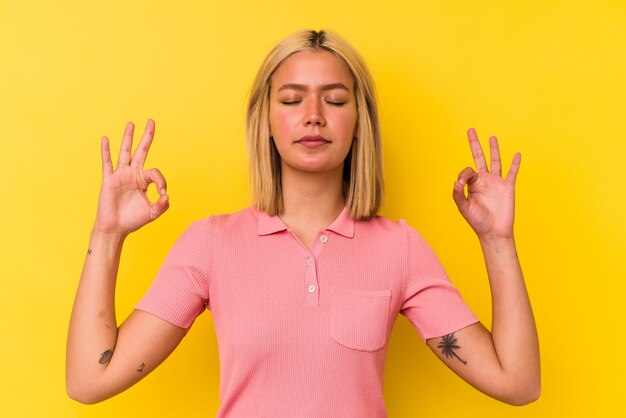 Jeune femme vénézuélienne isolée sur un mur jaune se détend après une dure journée de travail, elle effectue du yoga.