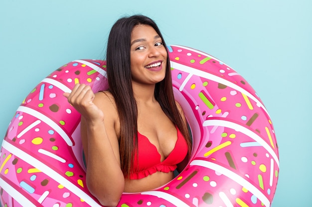 Jeune femme vénézuélienne tenant un beignet gonflable isolé sur des points de fond bleu avec le pouce loin, riant et insouciant.