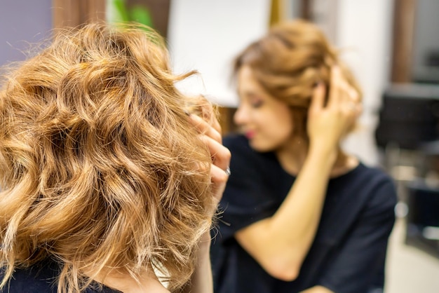 Jeune femme vérifiant sa nouvelle coiffure brune bouclée devant le miroir du salon de coiffure