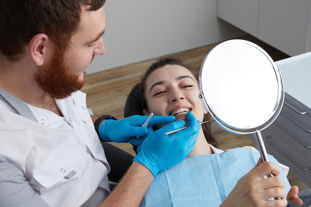 Jeune femme vérifiant son beau sourire dans le miroir après traitement stomatologique