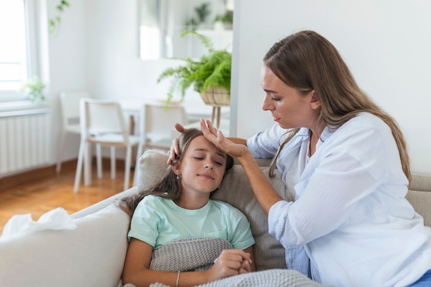 Jeune femme vérifiant la température avec la main de la petite fille malade. Mère vérifiant la température de sa fille malade. Enfant malade allongé sur le lit sous une couverture avec une femme vérifiant la fièvre sur le front à la main.