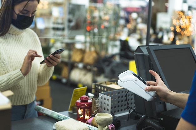 Jeune femme vérifie en utilisant le téléphone via le terminal dans le magasin distanciation sociale