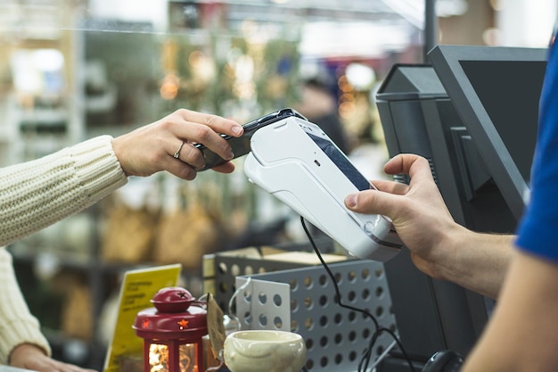 Jeune femme vérifie en utilisant le téléphone via le terminal dans le magasin distanciation sociale