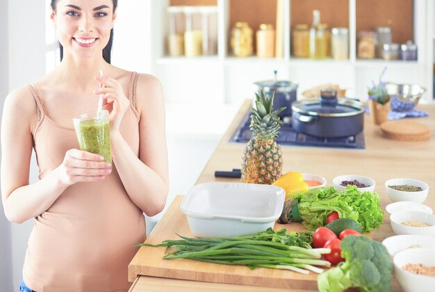 Jeune femme avec un verre de délicieux smoothie sain à table dans la cuisine