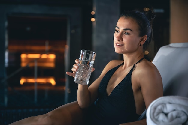 Une jeune femme avec un verre d'eau après le sauna se repose