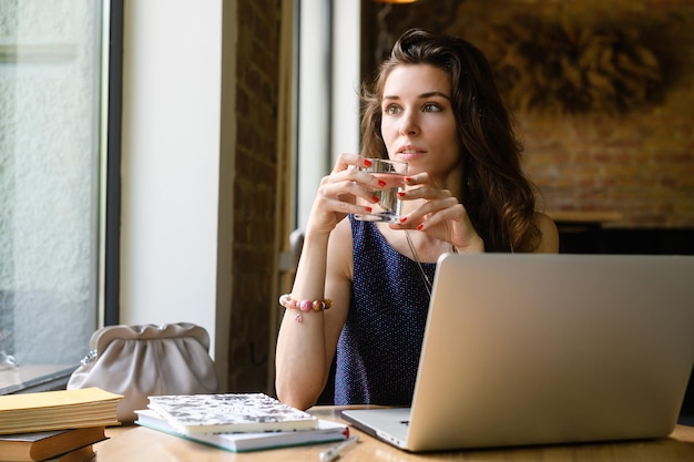 Une jeune femme avec un verre d'eau regarde par la fenêtre