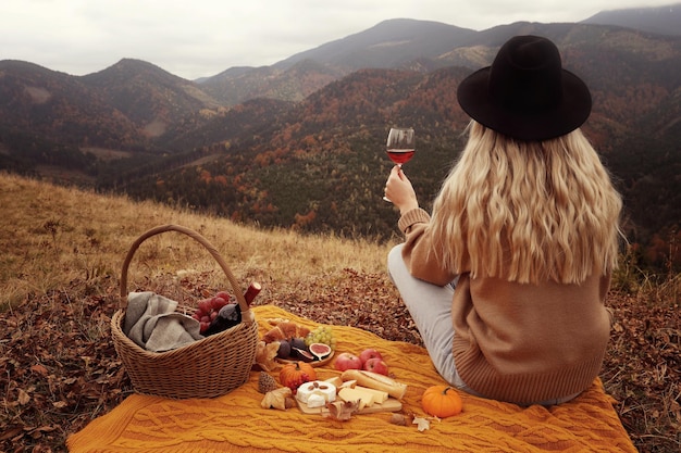 Jeune femme avec un verre de vin en train de pique-niquer dans les montagnes le jour de l'automne vue arrière