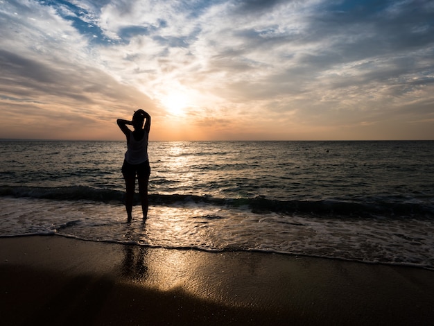 Jeune femme vers le magnifique coucher de soleil sur la plage de la mer. Profiter de l'instant