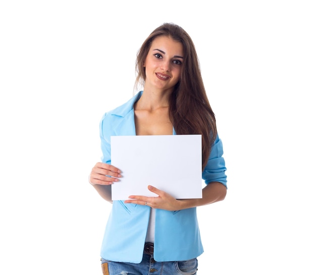 Jeune femme en veste bleue et jeans tenant une feuille de papier blanche sur fond blanc en studio