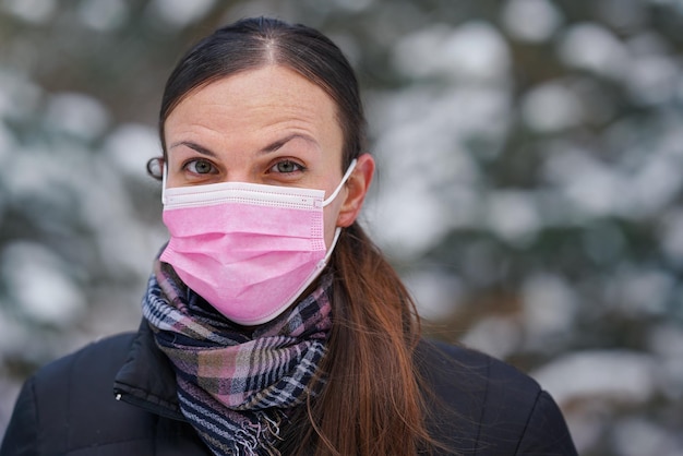 Jeune femme en veste d'hiver avec masque anti-virus facial jetable rose à usage unique