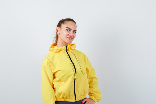 Jeune femme en veste jaune posant et semblant heureuse, vue de face.