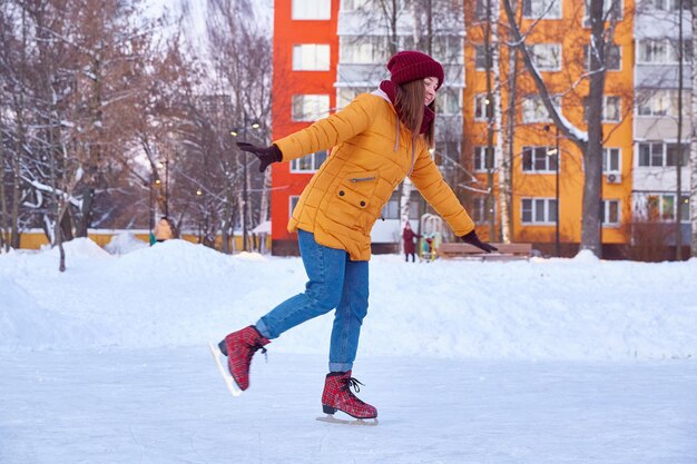 Une jeune femme en veste jaune roule sur de la glace sur un lac dans la cour d'immeubles à plusieurs étages