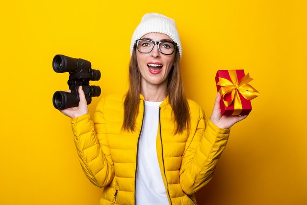 Jeune femme en veste jaune tenant un cadeau et des jumelles