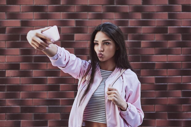 Jeune femme en veste rose debout isolé sur mur se prenant soi-même