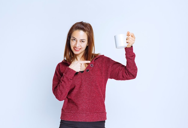 Jeune femme en veste rouge tenant une tasse de café blanche