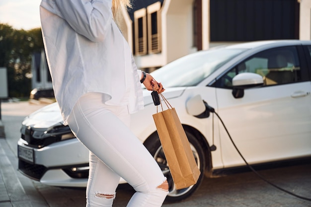 Jeune femme en vêtements blancs est avec sa voiture électrique pendant la journée