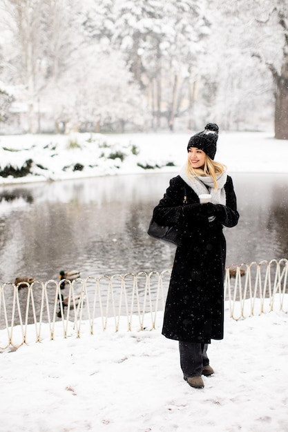 Jeune femme en vêtements chauds profitant de la neige avec une tasse de café à emporter