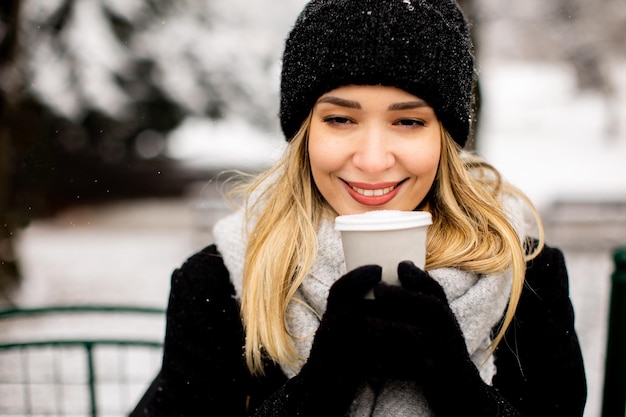Jeune femme en vêtements chauds profitant de la neige avec une tasse de café à emporter