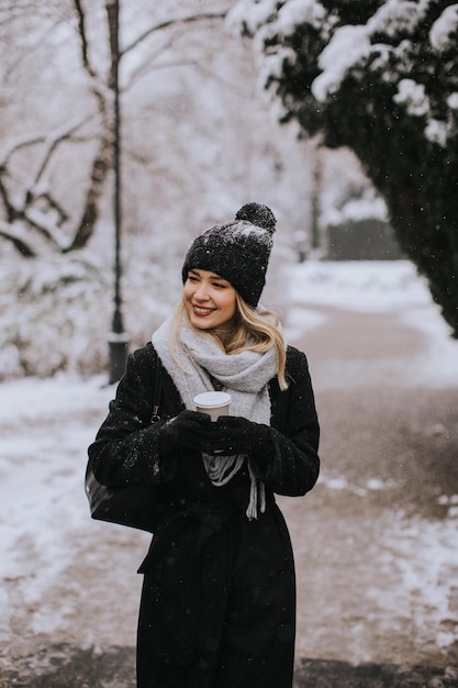 Jeune femme en vêtements chauds profitant de la neige avec une tasse de café à emporter