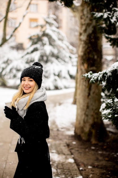 Jeune femme en vêtements chauds profitant de la neige avec une tasse de café à emporter