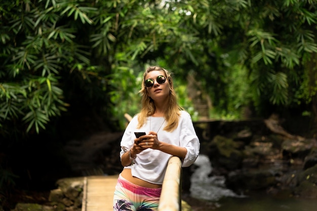 Une jeune femme en vêtements clairs et lunettes de soleil utilise un smartphone