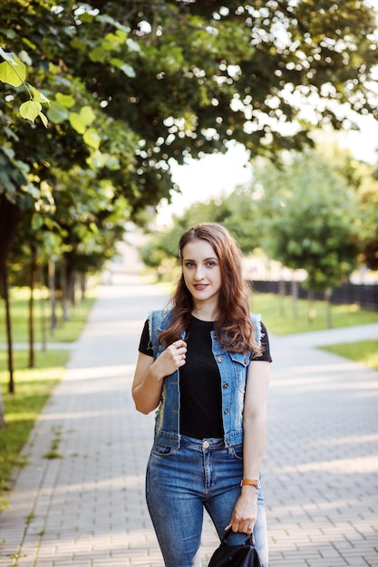 Jeune femme en vêtements décontractés t-shirt noir veste en jean et jeans passer du temps dans le parc en été