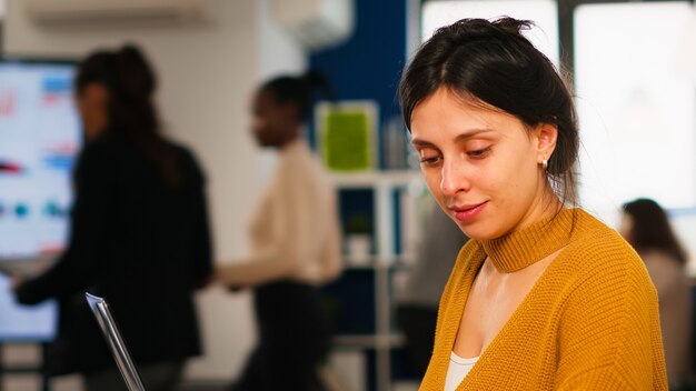 Jeune Femme En Vêtements Décontractés Travaillant Sur Un Ordinateur Portable Assis Au Bureau Dans Une Entreprise De Démarrage Financière Occupée Tandis Qu'une équipe Diversifiée Analyse Les Données Statistiques Dans Un Bureau Moderne. équipe Multiethnique Concentrée Sur Le Travail