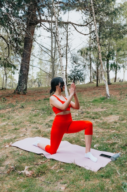 Jeune femme en vêtements de fitness faisant des exercices de yoga sur un tapis de yoga dans le parc pendant une journée ensoleillée