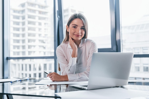 Jeune femme en vêtements formels blancs est à l'intérieur dans le bureau moderne