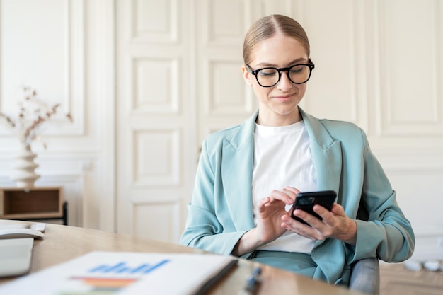 Une jeune femme en vêtements formels écrit un message à l'aide d'un téléphone au bureau