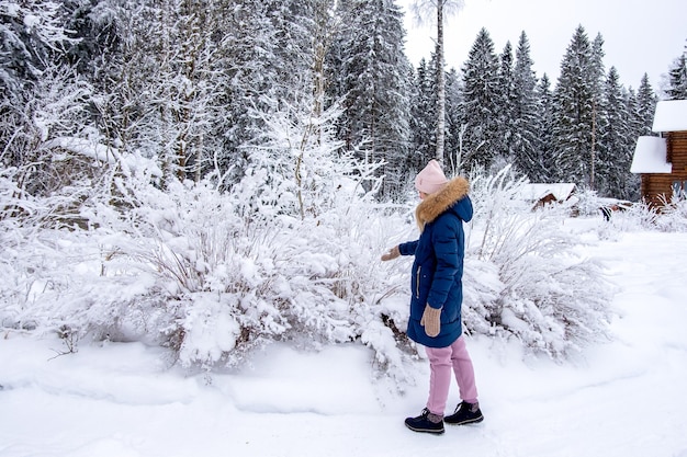 Une jeune femme en vêtements d'hiver chauds se promène parmi les buissons et les arbres couverts de neige dans la campagne