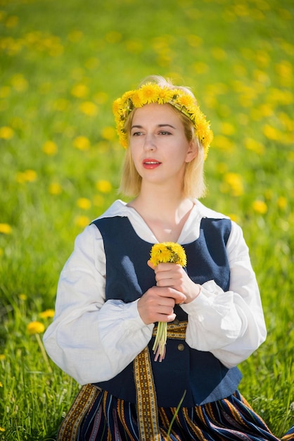 Jeune femme en vêtements nationaux portant une couronne de pissenlit jaune au printemps champ ligo