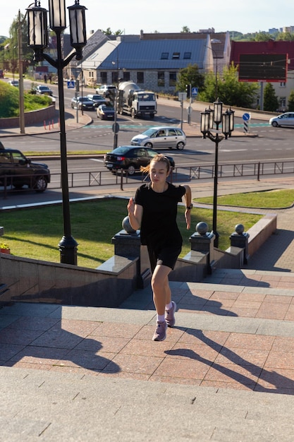 Une jeune femme en vêtements noirs courant sur les escaliers de la rue de la ville tôt le matin