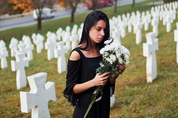 Jeune femme en vêtements noirs visitant le cimetière avec de nombreuses croix blanches Conception des funérailles et de la mort