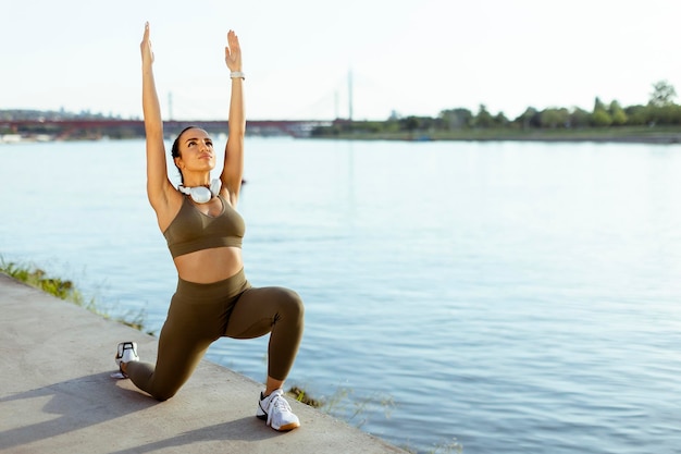 Jeune femme en vêtements de sport qui s'étend sur une promenade fluviale