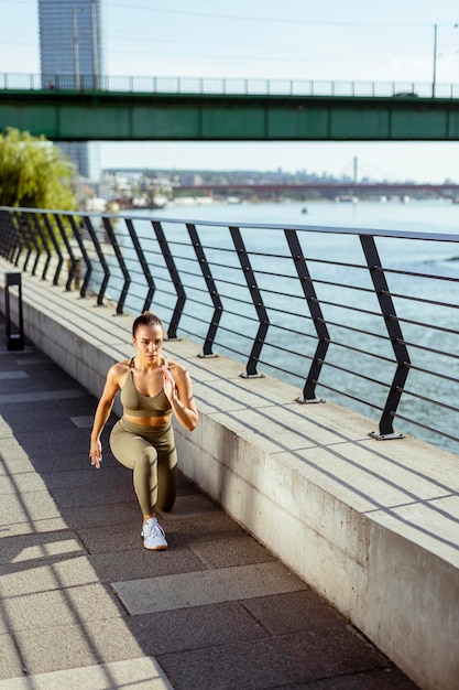 Jeune femme en vêtements de sport qui s'étend sur une promenade fluviale