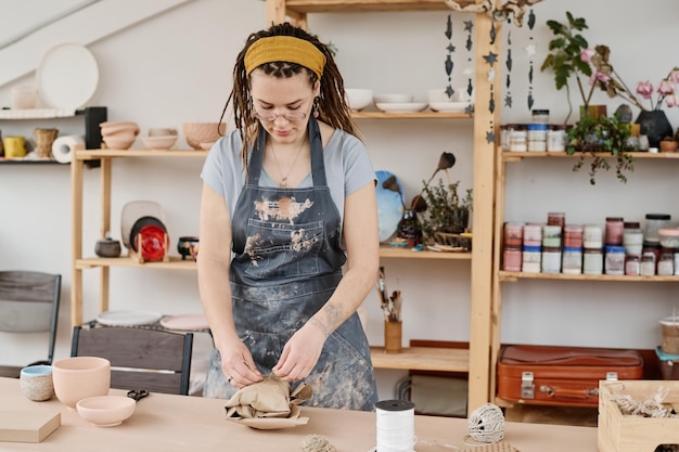 Jeune femme en vêtements de travail nouant un article en faïence emballé et emballé avec du fil