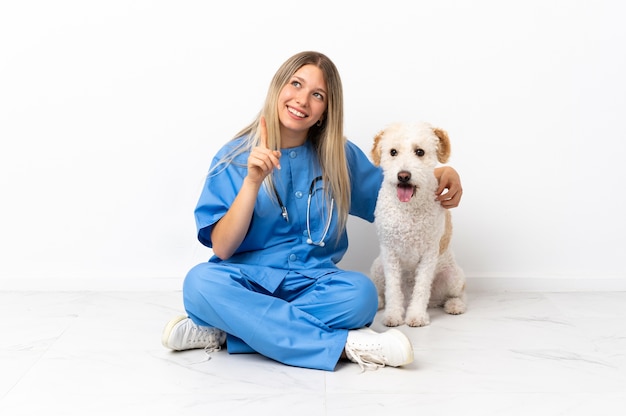 Jeune femme vétérinaire avec chien assis sur le sol pointant vers le haut une excellente idée