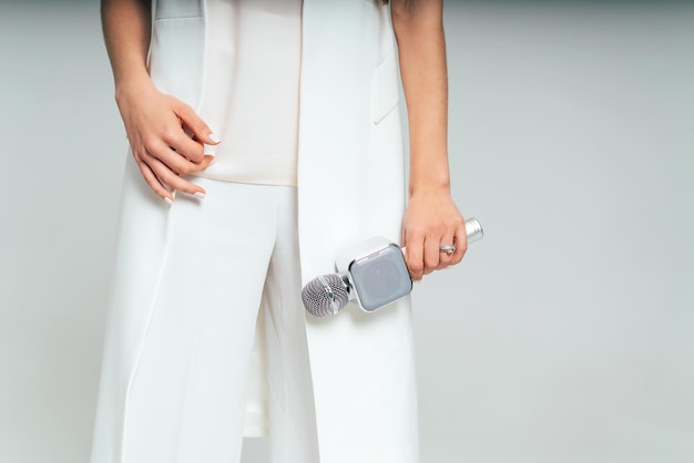 Jeune femme vêtue de blanc tenant dans les mains un microphone isolé sur un fond de studio gris Microphone et femme reporter méconnaissable en gros plan