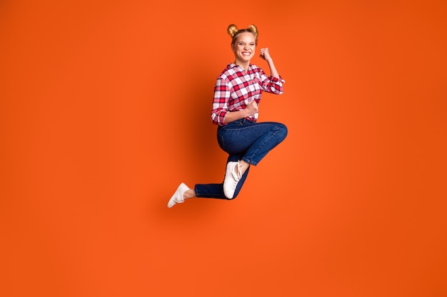 Jeune femme vêtue d'une chemise à carreaux à carreaux sautant et posant isolé sur orange