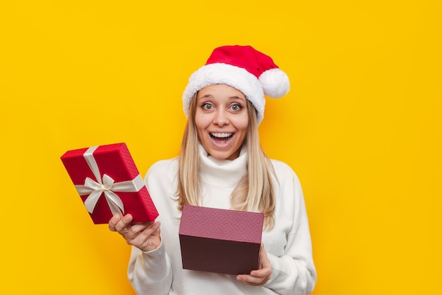 Une jeune femme vêtue d'un pull blanc de Noël et d'un chapeau de père Noël est heureuse du cadeau qu'elle a reçu